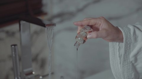 Woman's Hand Pouring Clear Liquid Soap Into Bathtub Preparing Fresh Bath Soak After A Long Day. - Close Up Shot