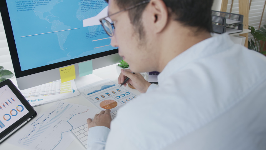 Over head shoulder back view of young attractive asian thai man busy work multiple screen computer or smart tablet on table desk at home in freelance data analyst, data science scientist for business. | Shutterstock HD Video #1062183433