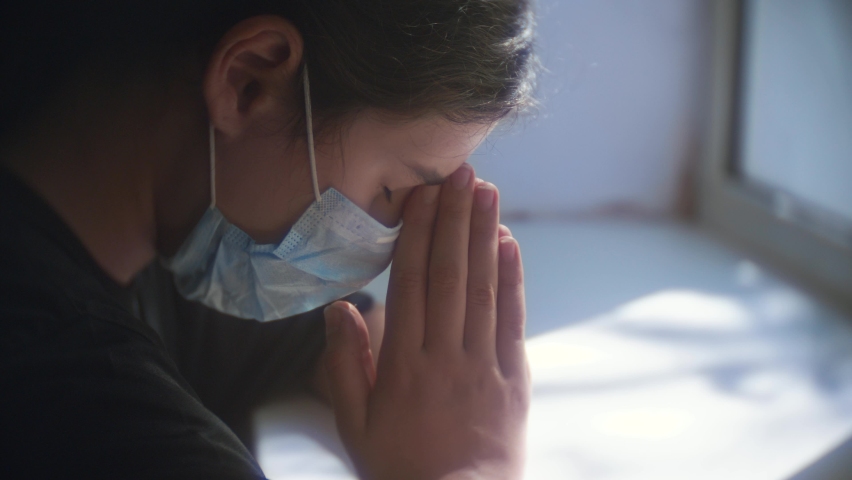 covid 19 religion concept. little girl looks out the window sad in a medical gauze mask. faith and religion doomsday self-isolation virus coronavirus pandemic infection. lonely little girl in Royalty-Free Stock Footage #1062185032