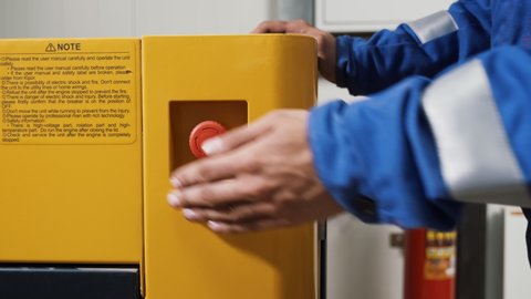 Hand of worker pushing red emergency button STOP. Equipment shutdown in case of breaking, or accident. Close up of hand turning off electrical industrial device. Danger of electricity.
