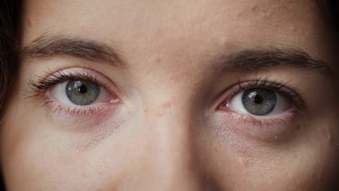 Close up of Woman's face. Attractive girl opening her beautiful blue eyes. Young female model with natural make-up and long eyelashes looking at camera. Slow-motion, macro extreme close-up, 4K.