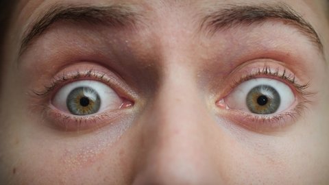 Close up of Man's face. Attractive boy opening his blue eyes in fear. Concept of shock, terror, horror. Male model with pretty blue, green, grey eyes. Slow-motion, macro extreme close-up, 4K.