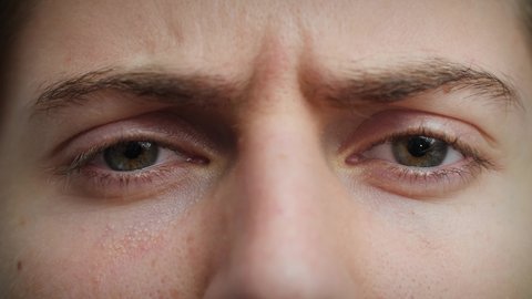 Close up of Man's face frowning. Boy with blue eyes looking at camera. Concept of disgust, anger, skepticism. Male model with pretty blue, green, grey eyes. Slow-motion, macro extreme close-up, 4K.