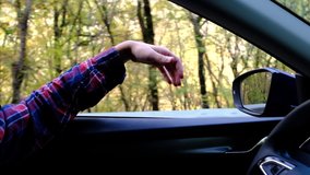 Cinematic inspirational video of young man travelling by car or camper van, opens window to breathe fresh air of countryside, moves hand in wind. Sings melody of song, autumn vacation vibes