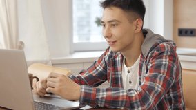 Happy young man student speaking to friends through laptop,  making video conference call looking at laptop writing notes talking by webcam sell online work from home, distant study online