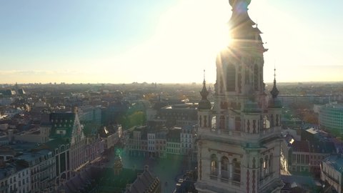 France, North, Lille, sun passing behind a close up of the belfry of the chamber of commerce during sunset (or sunrise) with Général De Gaulle Grand-Place in the background, drone aerial view.