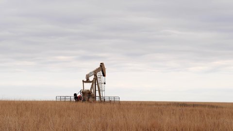 OSAGE CO., OKLAHOMA - 2 MAR 2020: Oil Well Pump Jack pumping crude oil for fossil fuel energy. American Petroleum Oil and Gas Industry equipment extracting oil from a field on a prairie. Slow zoom in.