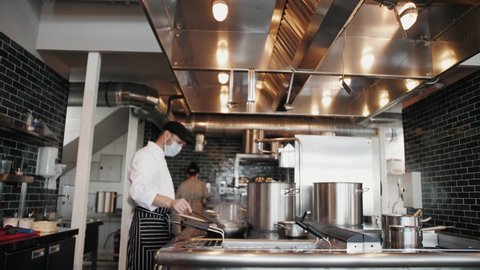 Chefs in protective masks and gloves prepare food in the kitchen of a restaurant or hotel, high kitchen during coronavirus covid 19 pandemic, business reopen after quarantine.