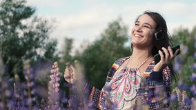 Beautiful young happy woman in headphones dancing in a purple field of lupine flowers