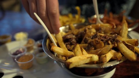 This delicious close up food video shows an anonymous hand grabbing gravy poutine covered french fries and dipping them in sauces.