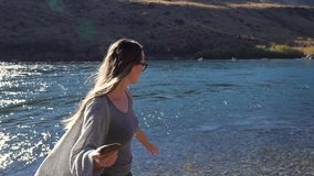 This serene slow motion video shows a young caucasian woman skipping a rock in a beautiful river and celebrating with joy afterwards.