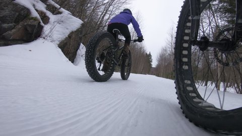 Biking in winter on fat bike. Woman fat biker riding bicycle in the snow in winter. Close up action shot of fat tire bike wheels in the snow. People living active winter sports lifestyle