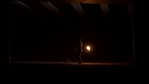 The man kicks a rope with a flame at the end. The rope flies far away and returns. Fire-show. Night performance. Slow motion