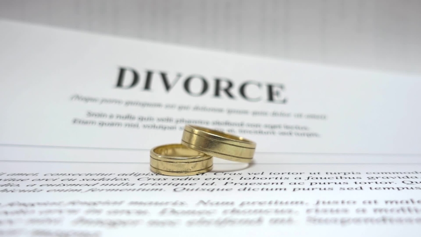 Conceptual video for divorce with two golden wedding ring in the middle and petition for divorce as background. Soft focus. Blurred divorce contract papers with wedding jewelry. | Shutterstock HD Video #1062212989