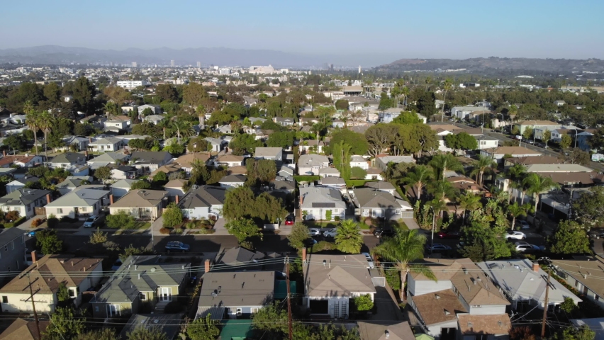 Aerial flyover over streets and neighborhood houses in Los Angeles suburbs with mountains in the background, in California, USA, Sunset, drone shot