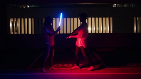 Couple in hats playing with lightsabers in the dark -wide