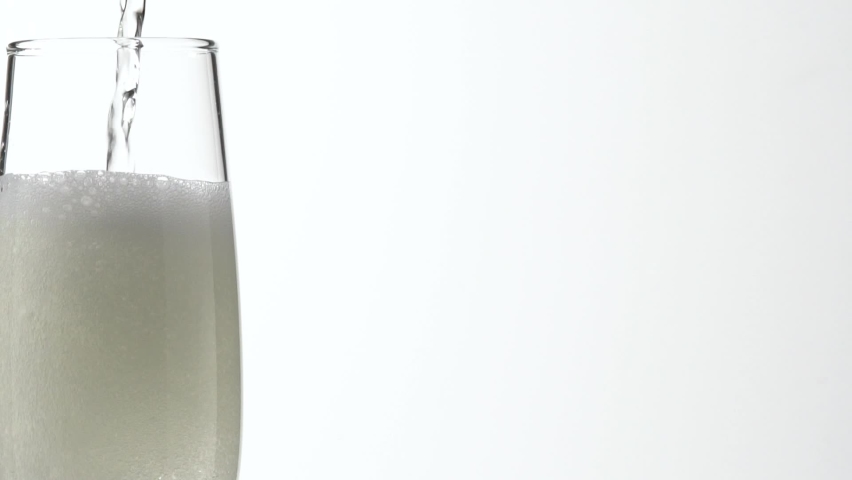 Jet Of Champagne Of Carbonated Drink Or An Alcoholic Cocktail Is Poured Into Glass On A White Background. Concept Of Tasting Alcoholic And Non-alcoholic Beverages In Cafes Bars And Restaurants