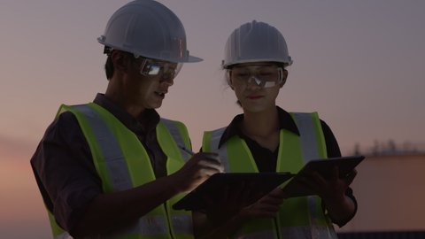 two Asian engineer using a digital tablet at the petroleum oil refinery in night shift