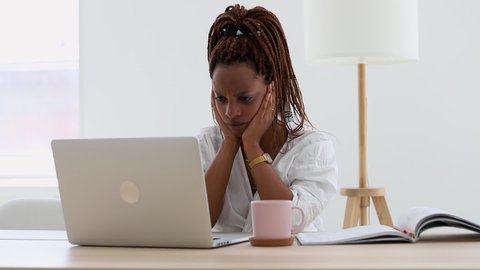 Sad African woman reading receiving bad pandemic news on a laptop at home. look computer screen and thinking about the problem of freelance. stressed frustrated female on white background.  