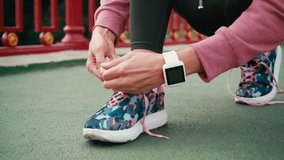 Cropped view of woman with smartwatch tying laces of sneaker on bridge