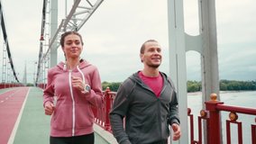 Smiling runners looking at each other, jogging and giving high five on bridge