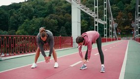Man and woman in sportswear stretching on bridge with nature on background