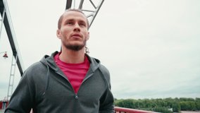 Focused man in sportswear running on bridge with cloudy sky on background