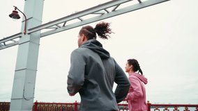 Smiling couple with smartwatches running on bridge with cloudy sky on background
