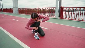 Female runner with smartwatch touching aching leg while sitting on bridge path