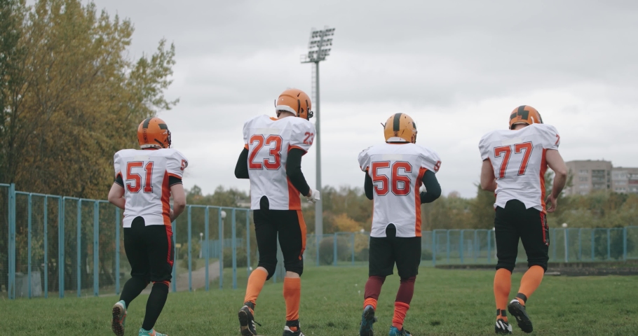 American football training day, athletic football players gets hug and high-five each other, after the winning match, the opposing team walk on the stadium in the background, 4k slow motion.