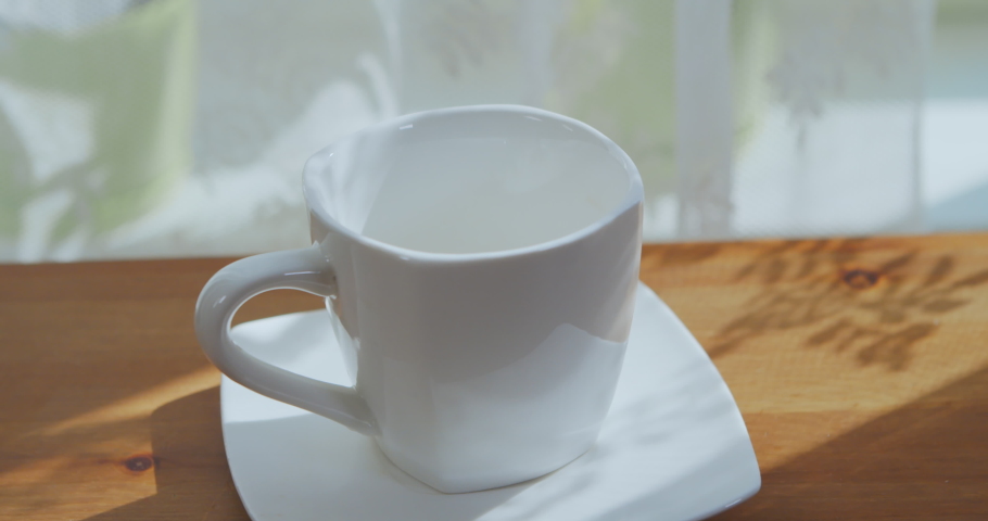 Man's hand pours coffee into a cup on a wooden table by the window. Drink fresh coffee in the morning at home. Man pours hot aromatic coffee into a white cup from a coffee machine in the room.  | Shutterstock HD Video #1062225214