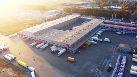 Logistics park with a warehouse - loading hub. Semi-trailers trucks standing at the ramps for loading/unloading goods at sunset. Aerial hyper lapse (motion time lapse).