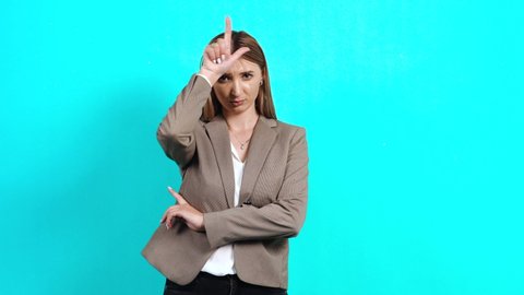 Upset young woman disappointed in business jacket, keeping her fingers near her forehead, showing the sign of lost sarcasm, unhappy because of the crisis. Studio image indoors, isolated on blue