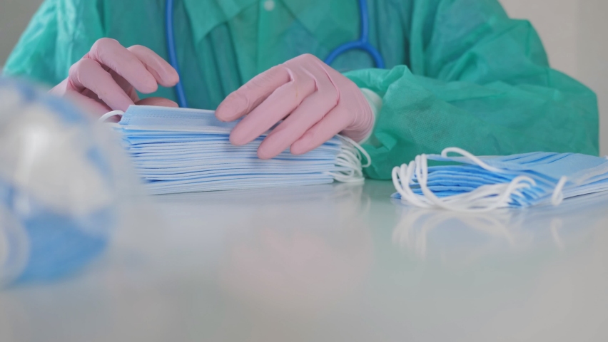 A female doctor in medical gloves is engaged in counting masks sitting at a table. Royalty-Free Stock Footage #1062228475