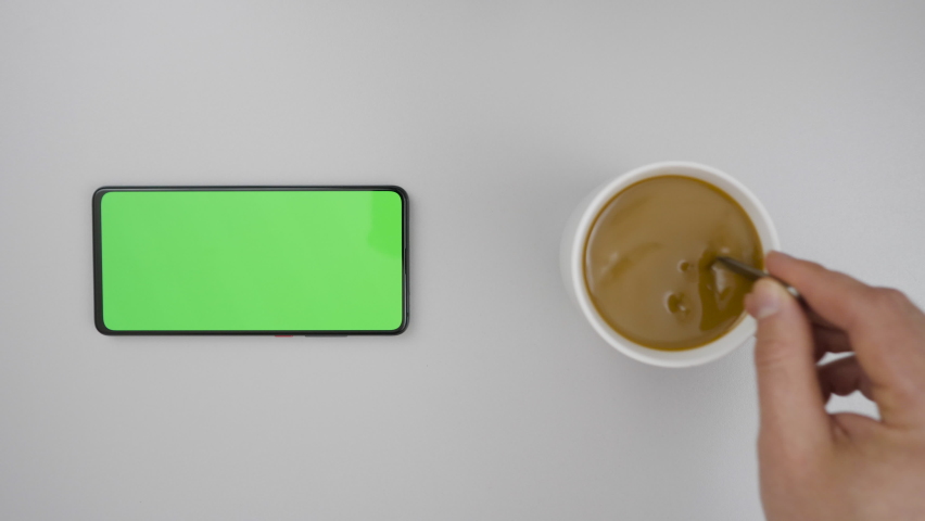 Smartphone with Green Mock-up Screen Business Concept. Person Hand Stirring Coffee with Spoon on Table. Slow Motion. | Shutterstock HD Video #1062228934