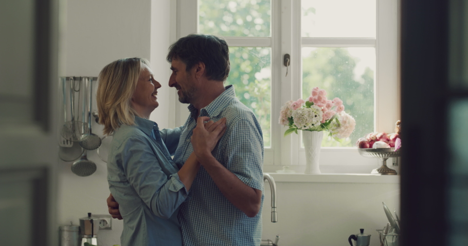 Cinematic shot of lovely happy mature couple is having fun dancing to celebrate their timeless love in a kitchen at home. 