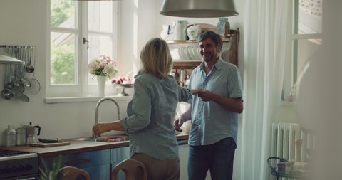 Cinematic shot of lovely happy mature couple is having fun dancing to celebrate their timeless love in a kitchen at home. 