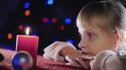 Girl dreamily looks at a candle on the background of the Christmas tree