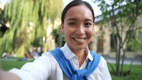 Cheerful asian woman having a video call, waving hand at camera and smiling outdoors. Point of view shot. Portrait.
