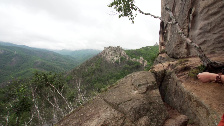 Travelling woman is coming in frame on the edge of high cliff and rising arms in joy. Beautiful landscape of endless forest. White City, Dragon Park in Russia