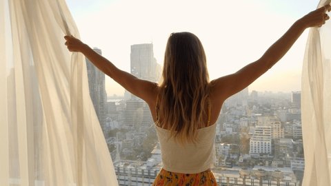 Woman opening curtains in hotel room at sunrise