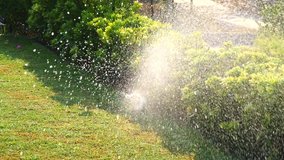 Automatic sprinkler system watering the lawn in sunshine in the garden on a background of green grass and villa, close-up. Summer watering of lawns. Slow motion video. Vacation season, drought.