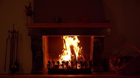 A 4k clip of a fire burning in a fireplace. On the right is a basket with more peaces of wood. This could also function as a screensaver.