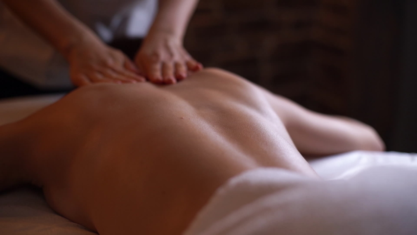 Young unrecognizable woman gets professional back massage in spa salon. Beautiful naked lady with perfect skin gets relaxing massage. Concept of luxury professional massage. Shooting in slow motion.