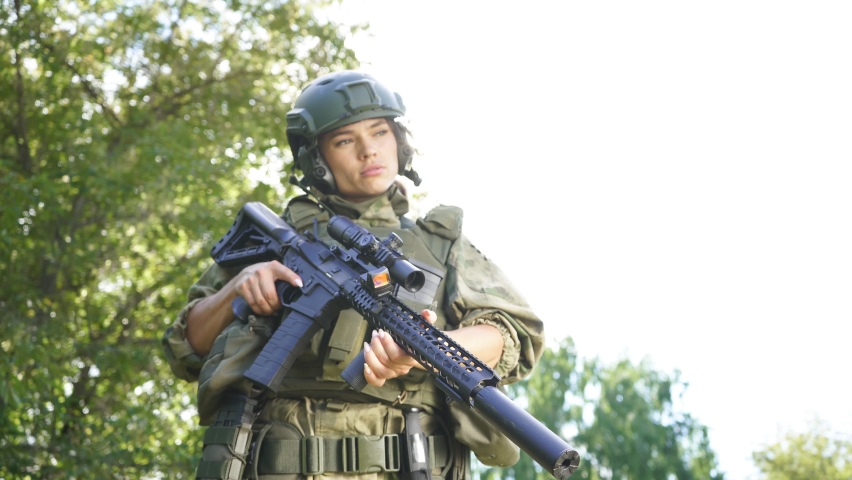 Portrait of confident military woman with a gun in forest, hunter female in camouflage suit with a gun stand in nature alone.