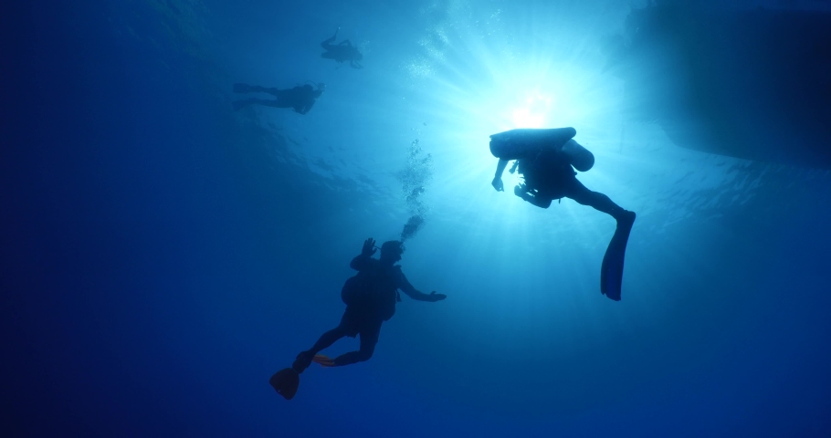 scuba divers ascending surface going back to boat underwater with sun beams and rays ocean scenery Royalty-Free Stock Footage #1062251002