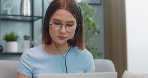 Close up of smart female support specialist in glasses teleworking at home. Attractive young woman consulting client via video conference on laptop. Service, technology, job concept.
