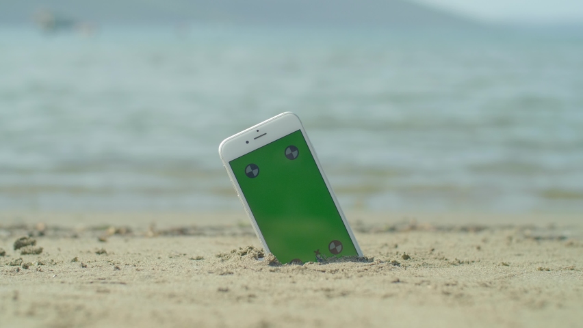 Mugla / Turkey - 09.29.2020 : Mobile phone in sand at beach with green screen, sea and tracking signs.