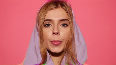 Portrait of young sexy playful blond woman dressed in blue hoodie  isolated over pink background blowing bubblegum candy bubbles and chewing gum.Model looking at camera. Glitch effect