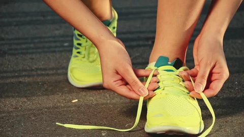 Slow motion: running shoes. Barefoot running shoes closeup. Female athlete tying laces for jogging on road in minimalistic barefoot running shoes. Runner getting ready for training. Sport lifestyle.